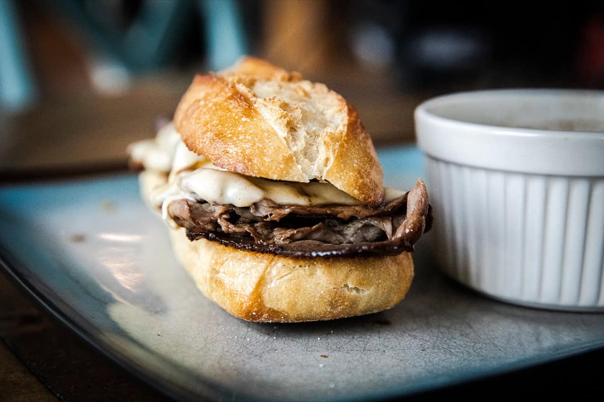 Close-up of a French dip sandwich with beef and melted cheese on a bun.