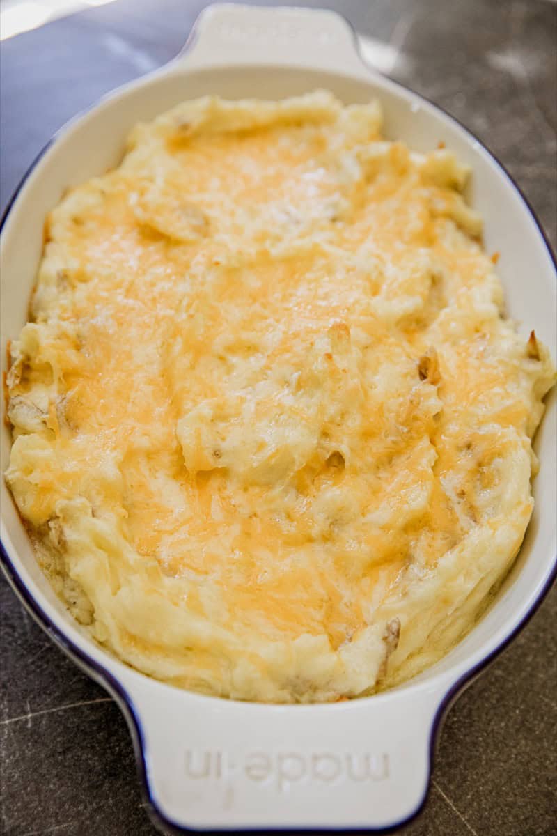 Creamy cheesy mashed potatoes topped with melted cheese in a baking dish.