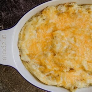 Creamy cheesy mashed potatoes topped with melted cheese in a baking dish.