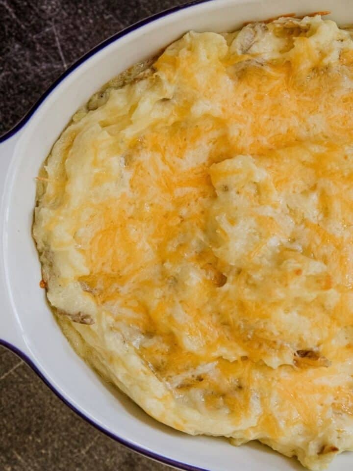 Creamy cheesy mashed potatoes topped with melted cheese in a baking dish.