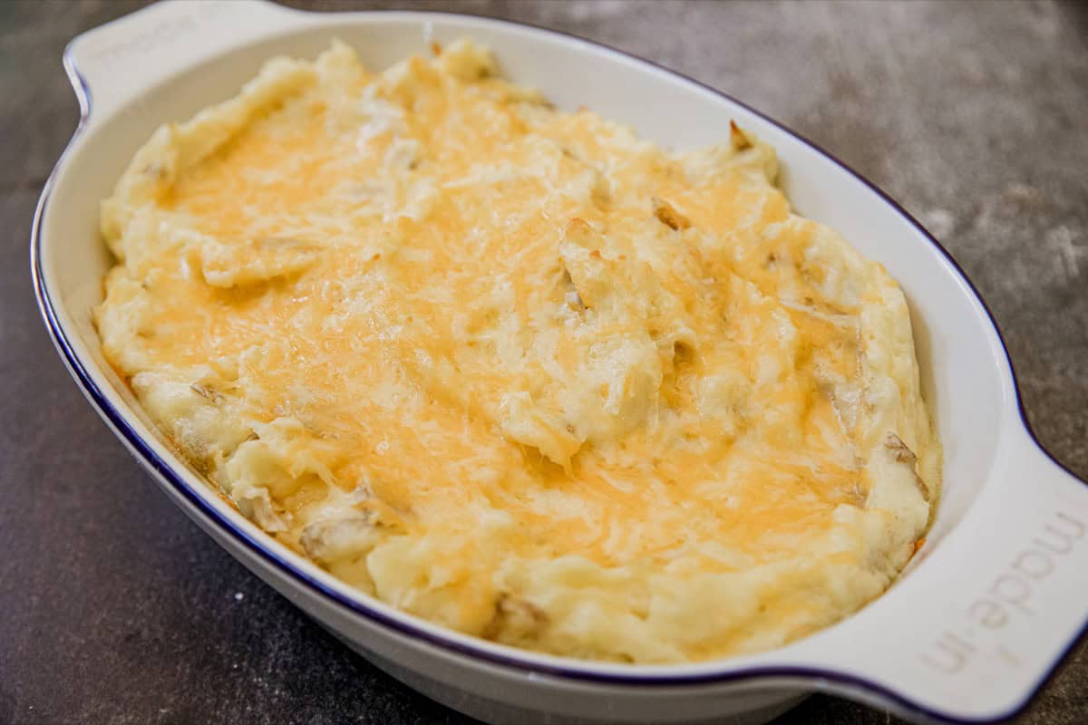 Creamy cheesy mashed potatoes in a white oval dish on a dark surface.