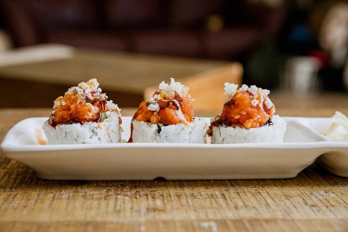 Spicy Dynamite Rolls with spicy sauce and toppings on white plate.