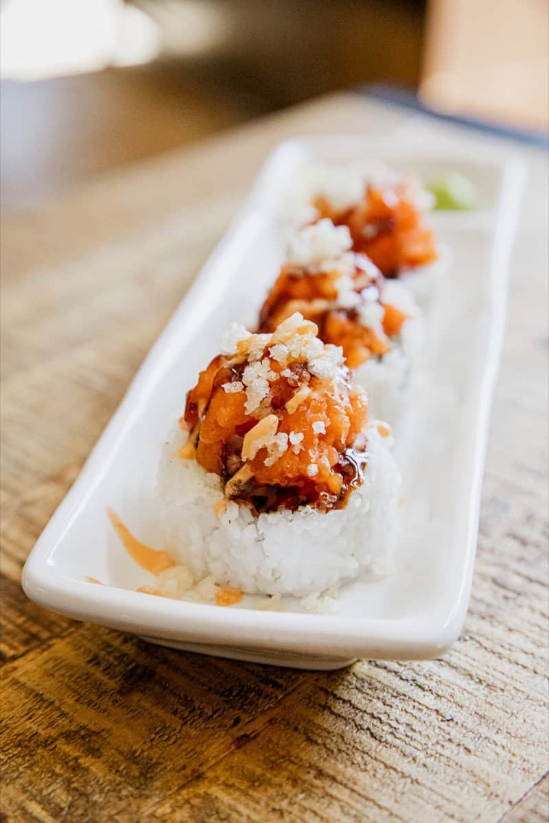 Close-up of spicy dynamite sushi rolls with toppings on a white plate.