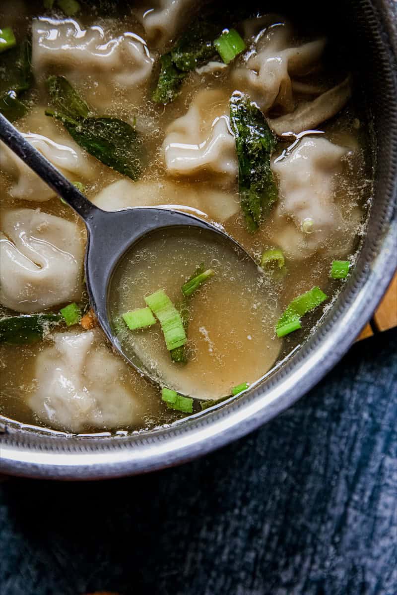 Close-up of chicken wonton soup with green onions in a pot.