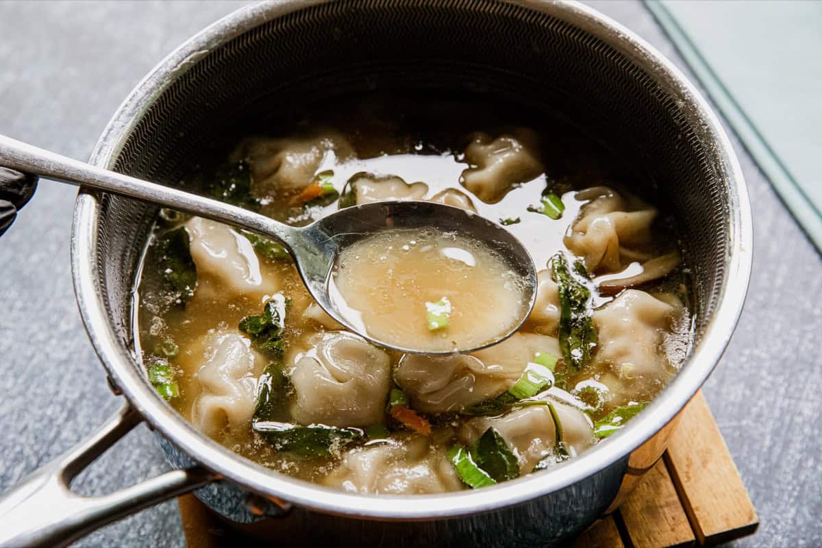 Close-up of chicken wonton soup in a pot with a spoon.