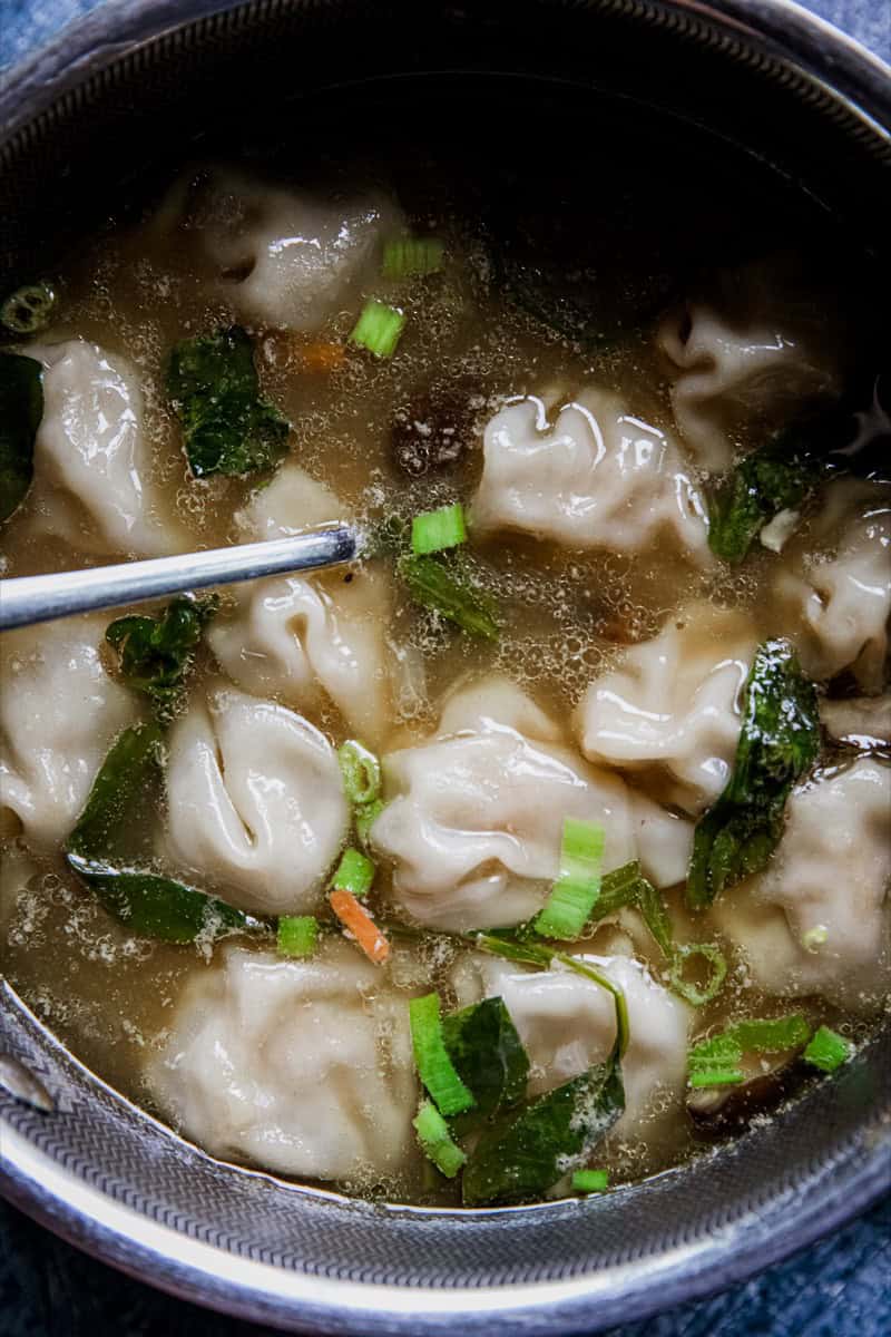 Close-up of chicken wonton soup with green onions in a black bowl.