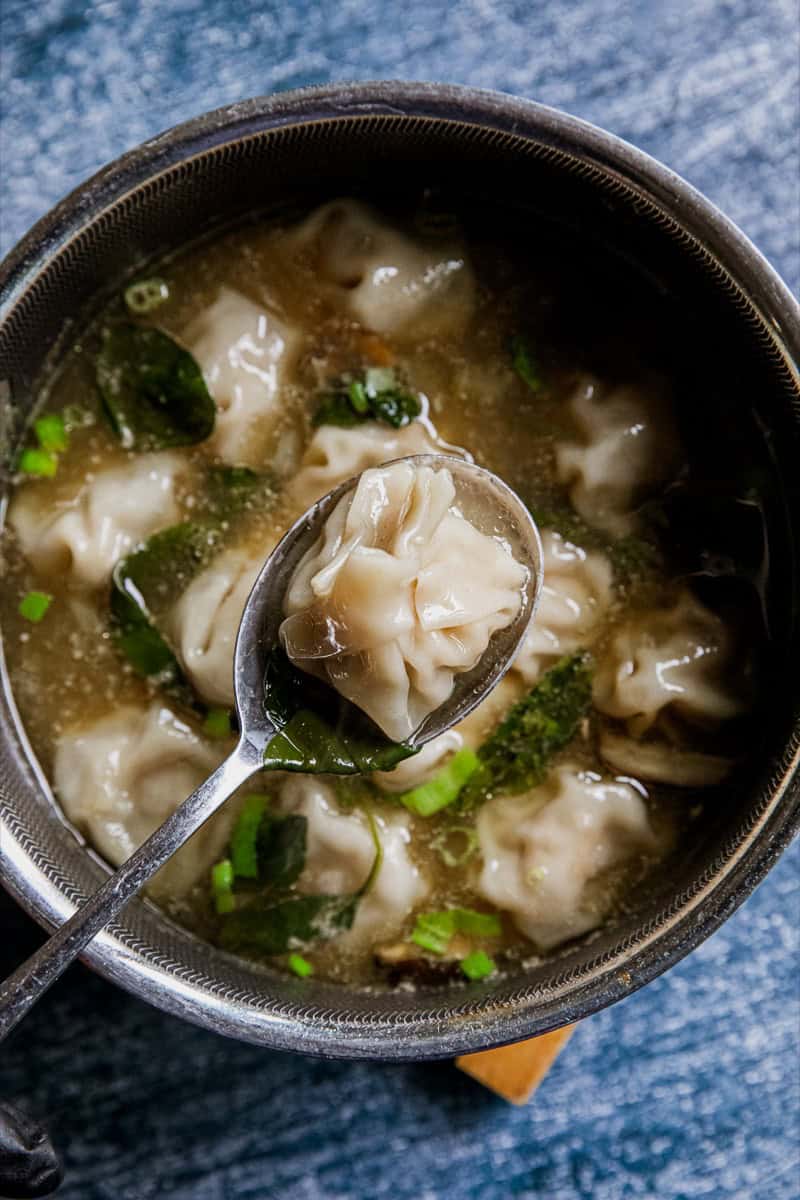 Close-up of chicken wonton soup with green onions in a bowl.