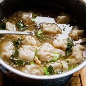 Close-up of chicken wontons in clear broth with green onions.