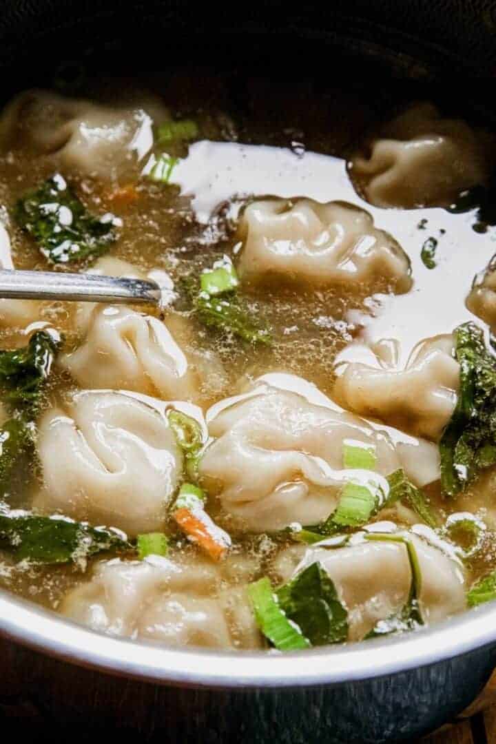 Close-up of chicken wontons in clear broth with green onions.