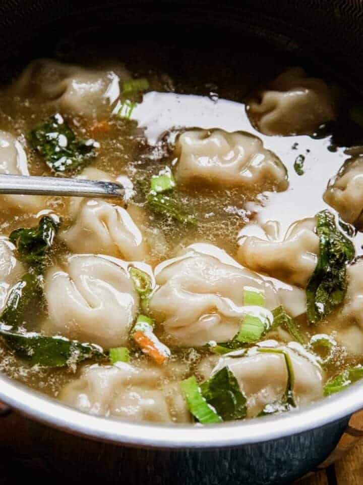 Close-up of chicken wontons in clear broth with green onions.