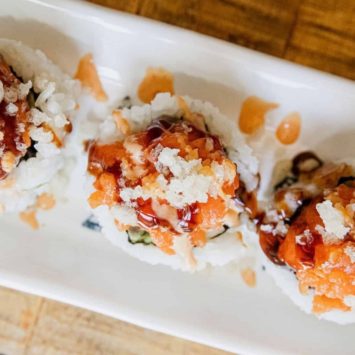 Close-up of spicy dynamite sushi rolls with sauce and toppings.
