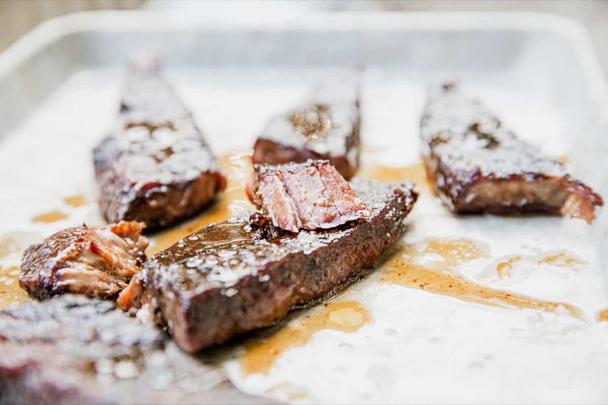 Juicy smoked boneless chuck short ribs on a tray with sauce.