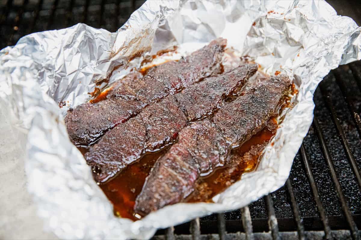 Juicy smoked boneless chuck short ribs in foil on grill.