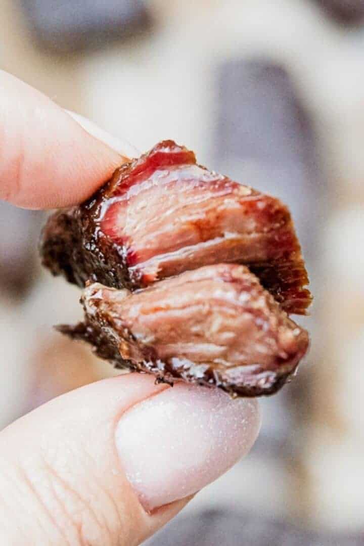 Close-up of smoked boneless chuck short ribs held between fingers.