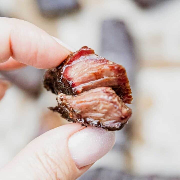 Close-up of smoked boneless chuck short ribs held between fingers.