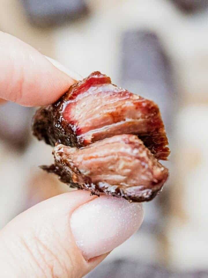 Close-up of smoked boneless chuck short ribs held between fingers.