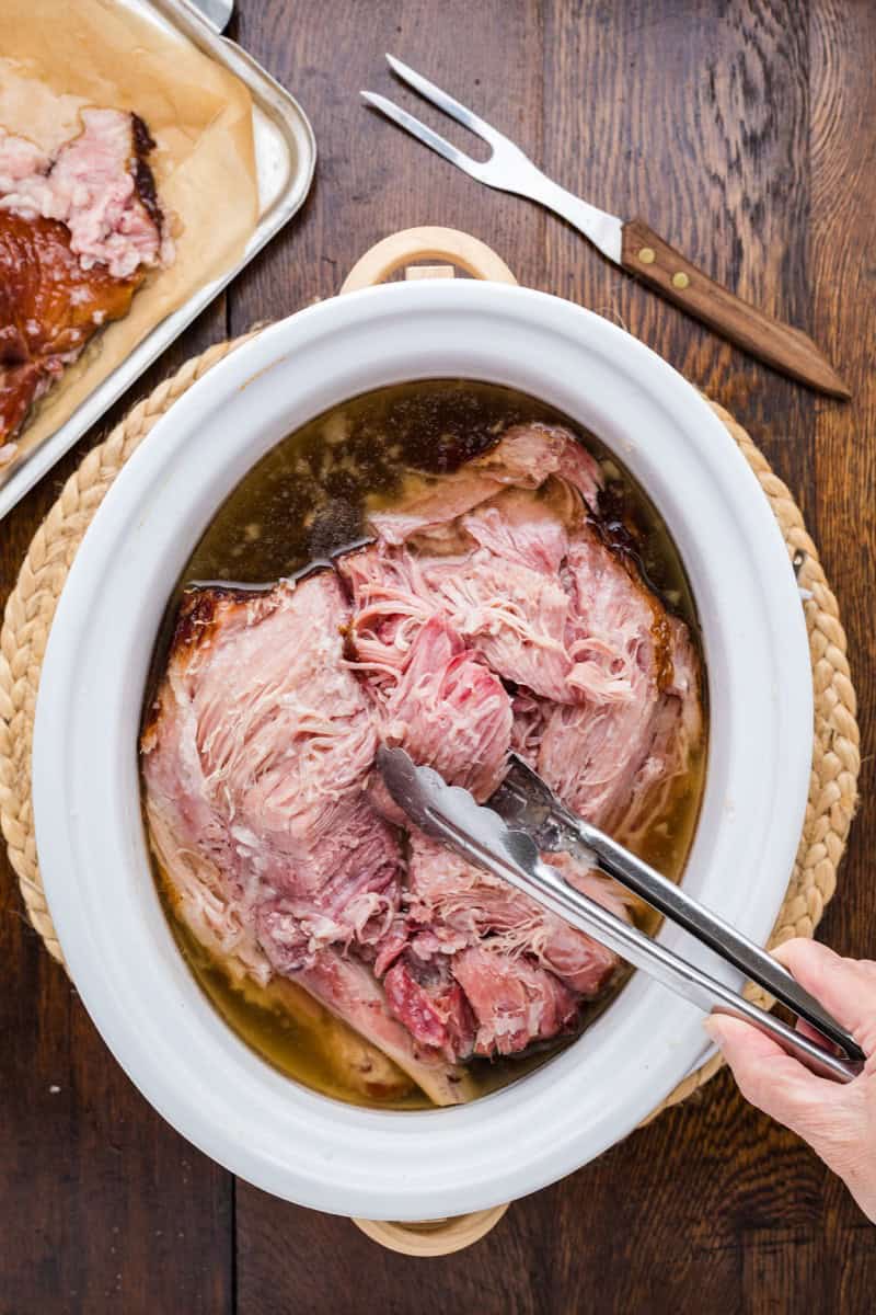 Juicy double smoked picnic ham in a white serving dish with tongs.
