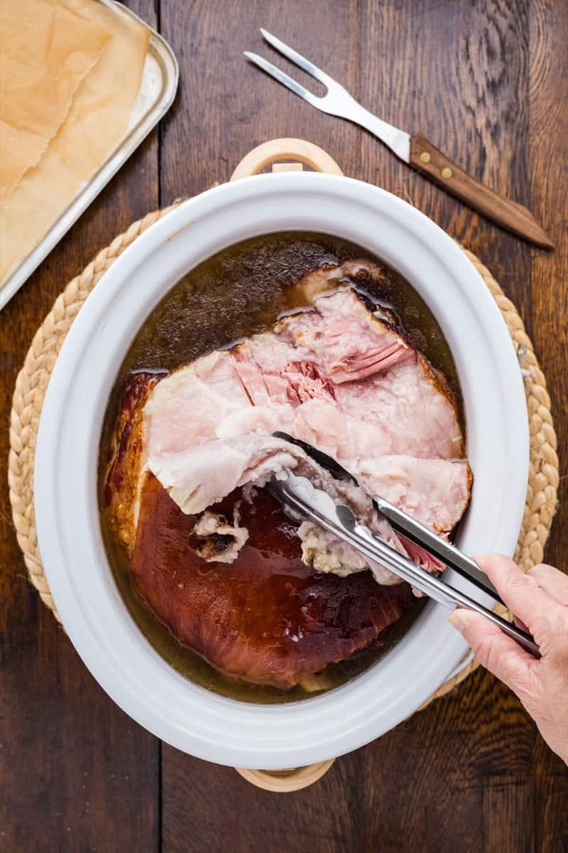 Cooking a double smoked picnic ham in a slow cooker with tongs.