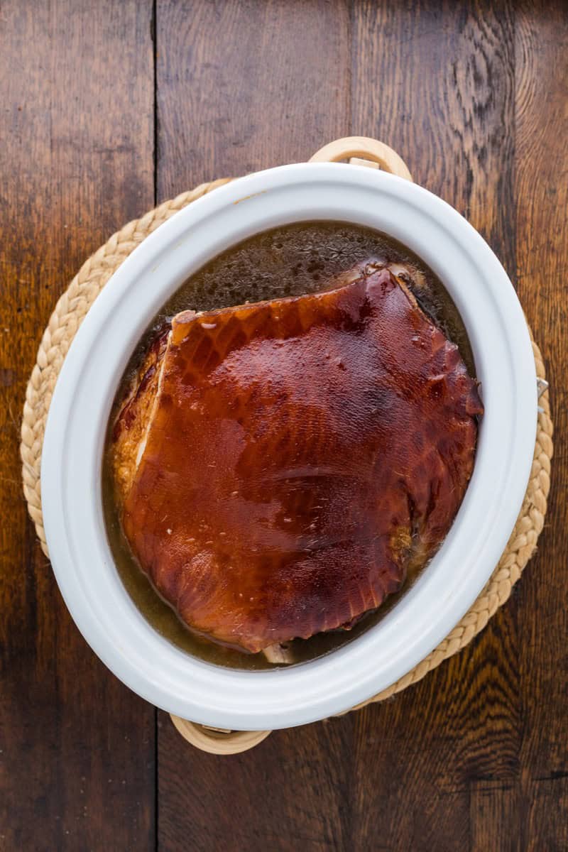 Juicy double smoked picnic ham in a white dish on wooden table.