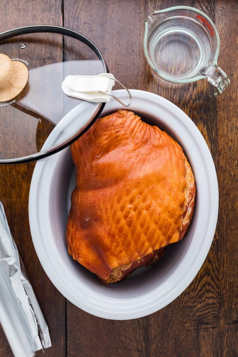 Juicy double smoked picnic ham on a white platter with cooking tools nearby.