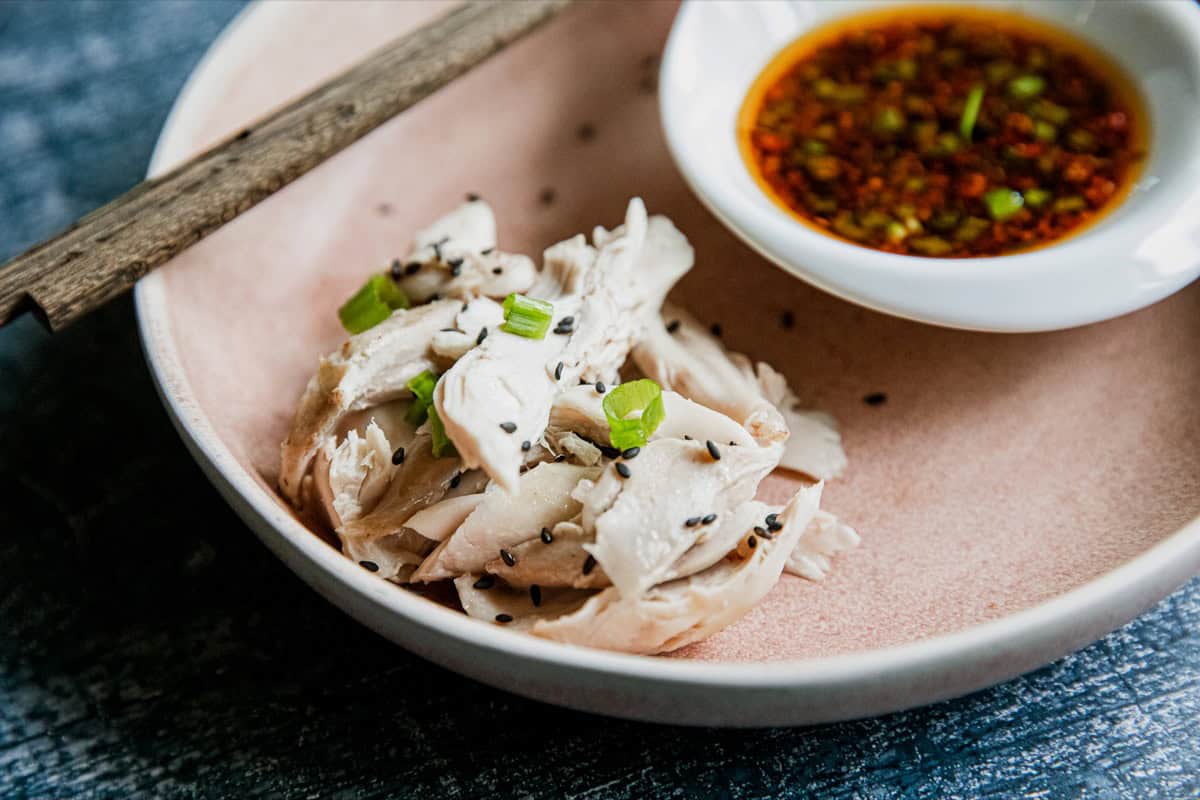 Steamed chicken slices with green onions and dipping sauce in a bowl.