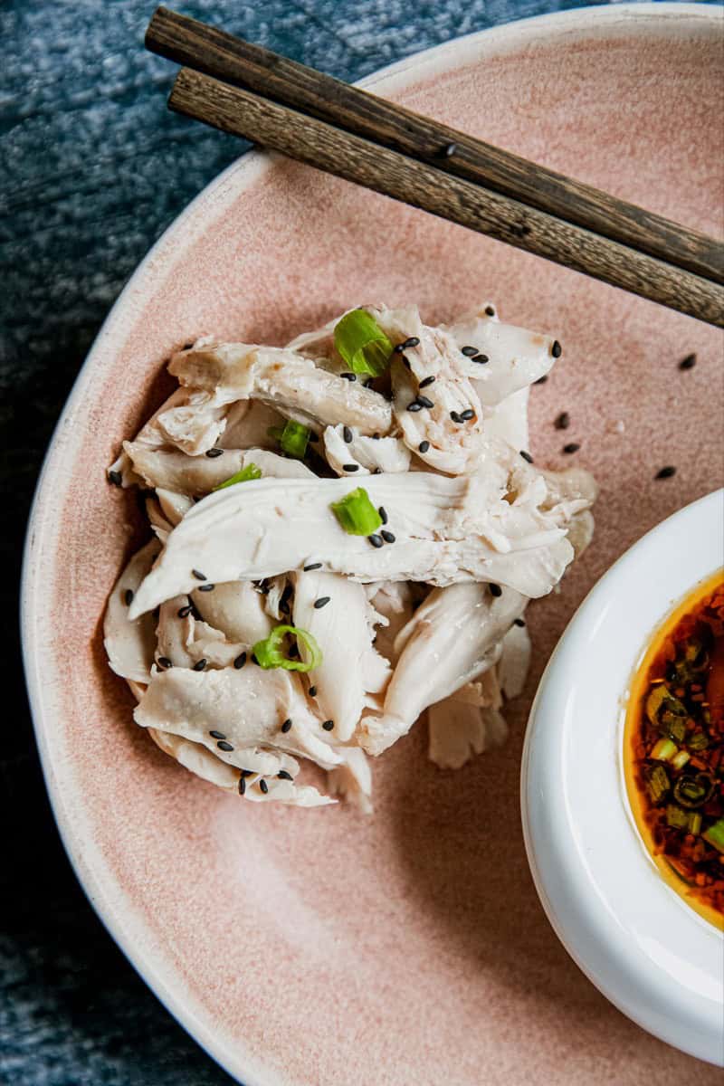 Steamed chicken slices garnished with green onions and black sesame seeds on a pink plate.
